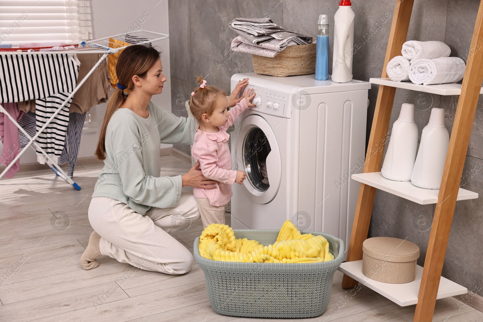 Photo of Housewife with her little daughter doing laundry at home