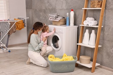 Photo of Housewife with her little daughter doing laundry at home