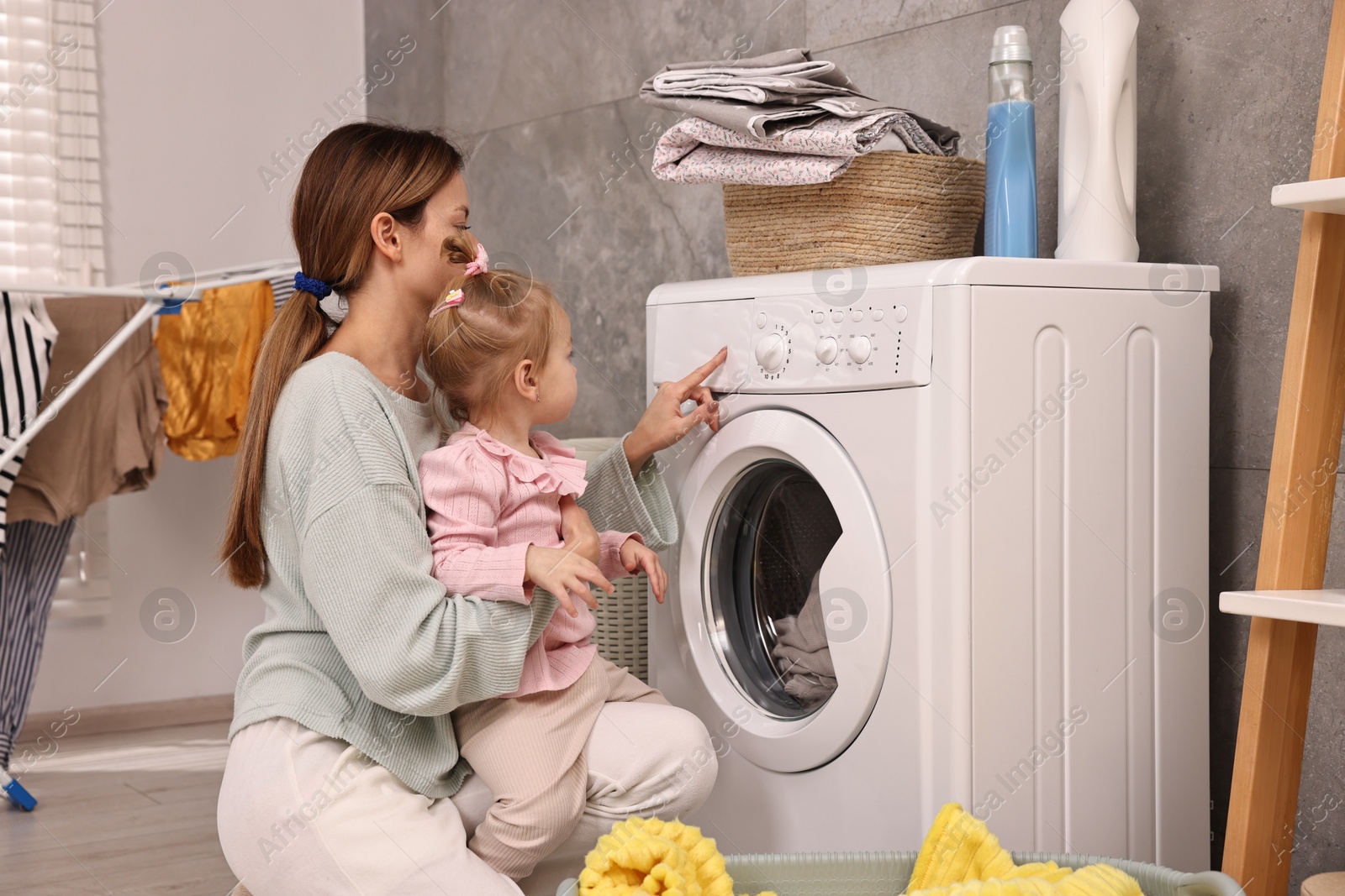 Photo of Housewife with her little daughter doing laundry at home