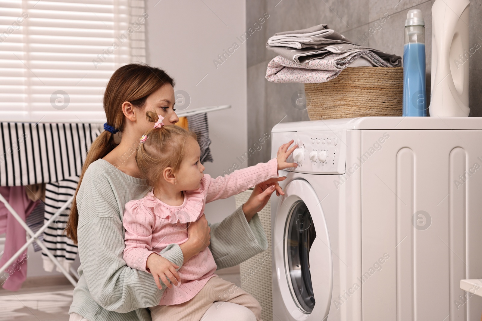 Photo of Housewife with her little daughter doing laundry at home