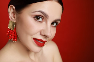 Photo of Beautiful young woman wearing elegant earrings on red background, closeup. Space for text