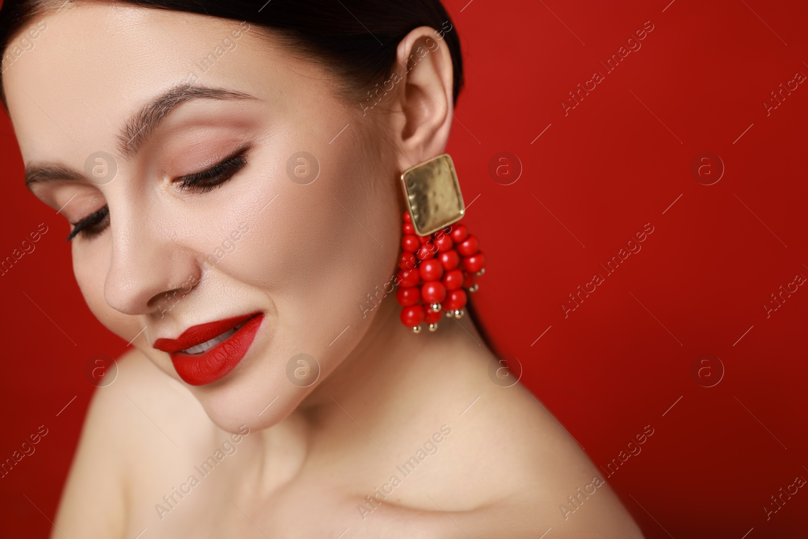 Photo of Beautiful young woman wearing elegant earrings on red background, closeup. Space for text