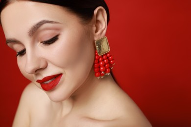 Photo of Beautiful young woman wearing elegant earrings on red background, closeup. Space for text