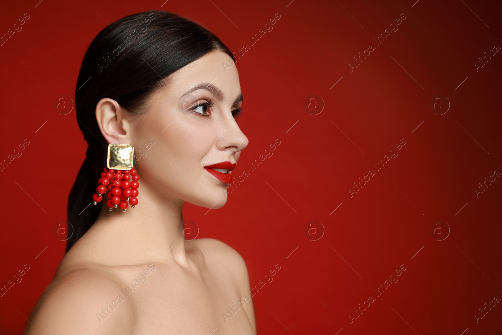 Photo of Beautiful young woman wearing elegant earrings on red background. Space for text