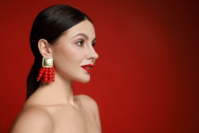 Beautiful young woman wearing elegant earrings on red background. Space for text