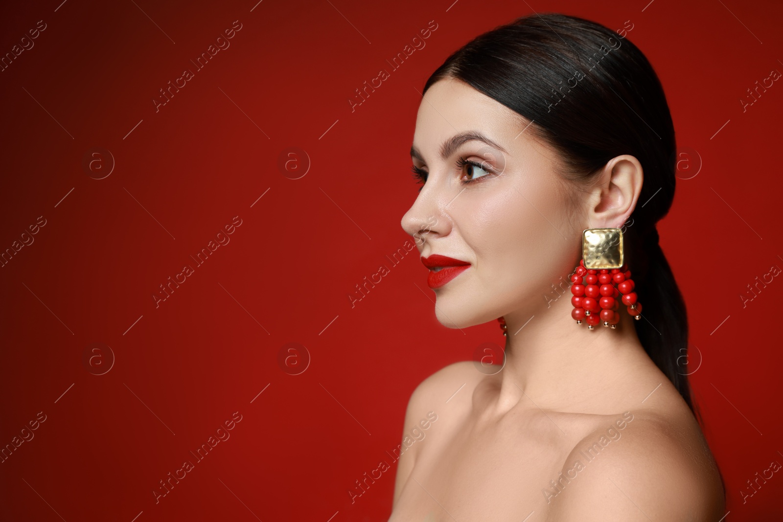 Photo of Beautiful young woman wearing elegant earrings on red background. Space for text