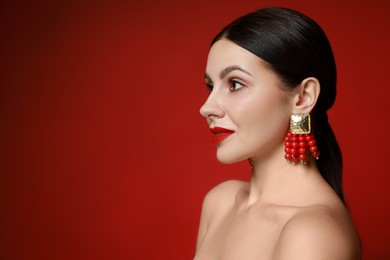 Beautiful young woman wearing elegant earrings on red background. Space for text