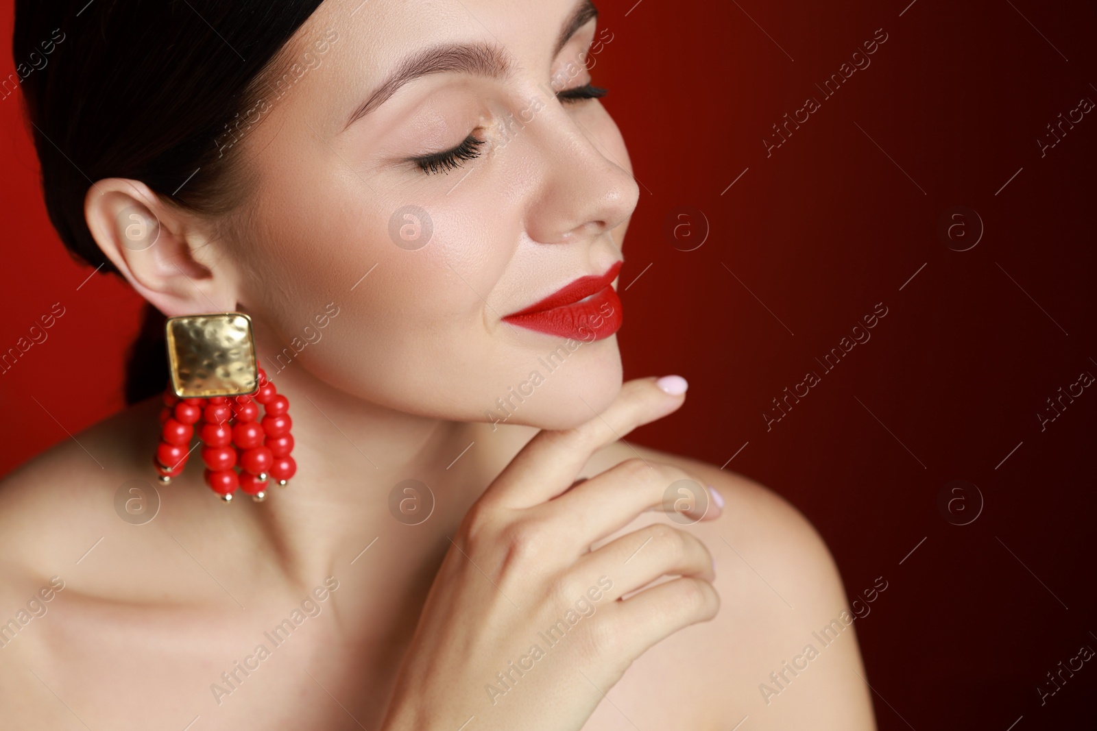 Photo of Beautiful young woman wearing elegant earrings on red background, closeup. Space for text