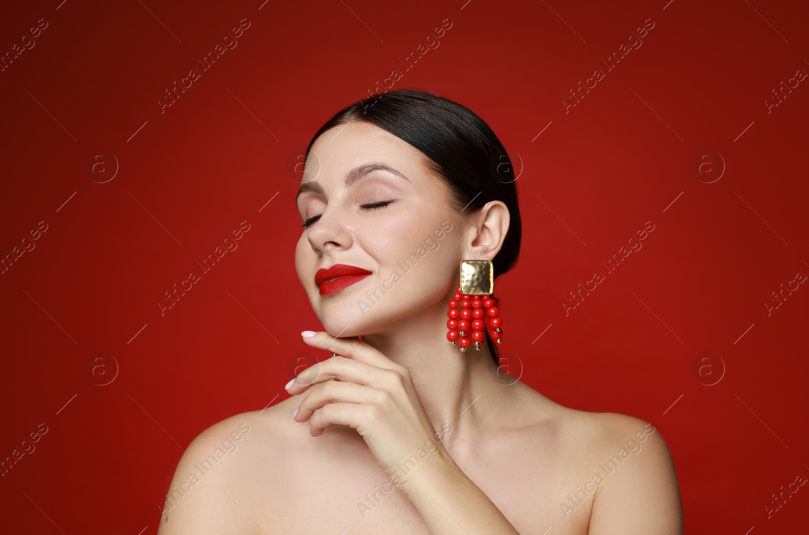 Photo of Beautiful young woman wearing elegant earrings on red background