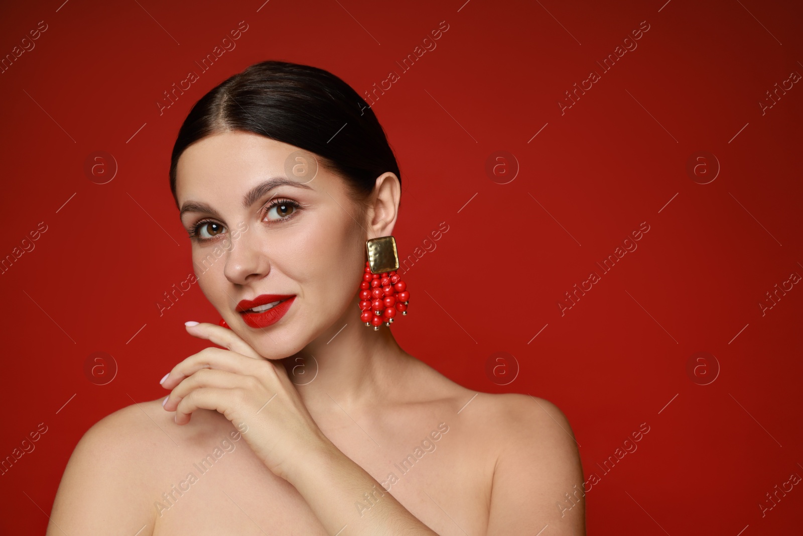 Photo of Beautiful young woman wearing elegant earrings on red background. Space for text