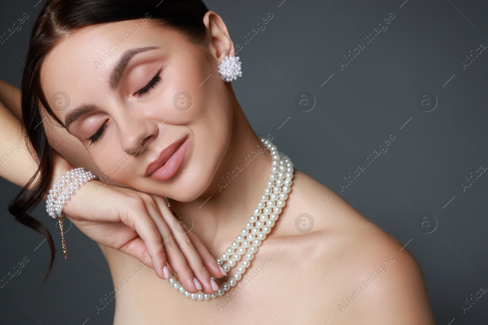 Photo of Beautiful young woman wearing elegant pearl jewelry on dark grey background, closeup. Space for text