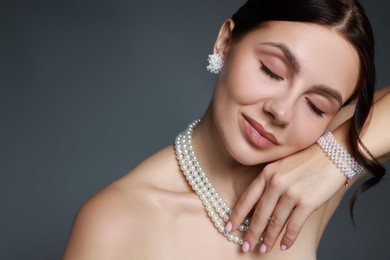 Photo of Beautiful young woman wearing elegant pearl jewelry on dark grey background, closeup. Space for text