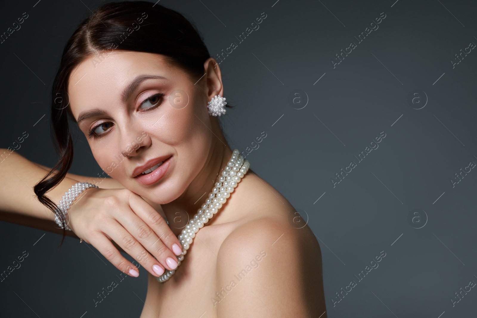 Photo of Beautiful young woman wearing elegant pearl jewelry on dark grey background. Space for text