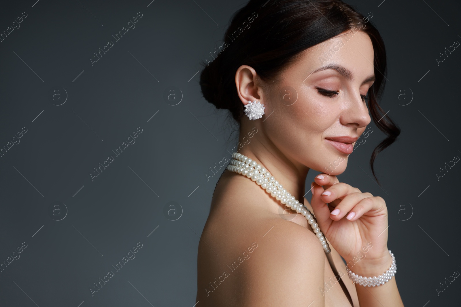 Photo of Beautiful young woman wearing elegant pearl jewelry on dark grey background. Space for text