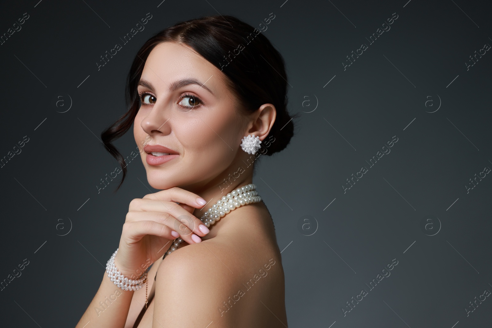 Photo of Beautiful young woman wearing elegant pearl jewelry on dark grey background. Space for text