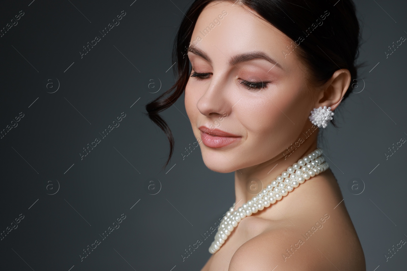 Photo of Beautiful young woman wearing elegant pearl jewelry on dark grey background, closeup. Space for text