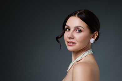 Photo of Beautiful young woman wearing elegant pearl jewelry on dark grey background. Space for text