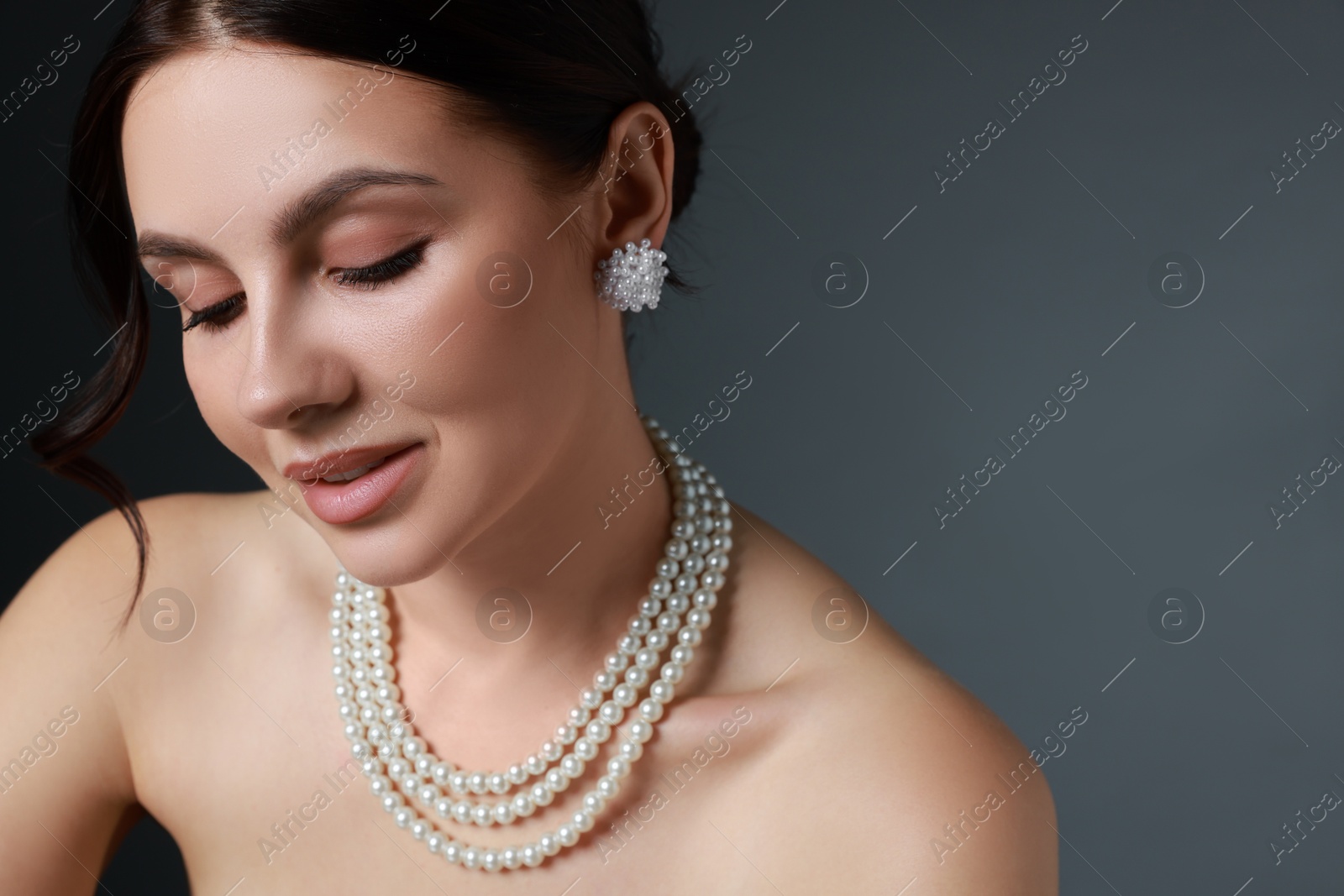 Photo of Beautiful young woman wearing elegant pearl jewelry on dark grey background, closeup. Space for text