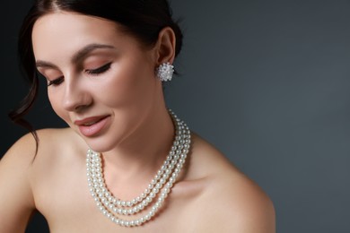 Beautiful young woman wearing elegant pearl jewelry on dark grey background, closeup. Space for text