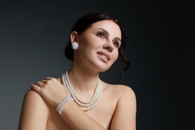 Photo of Beautiful young woman wearing elegant pearl jewelry on dark grey background