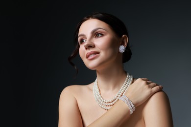 Photo of Beautiful young woman wearing elegant pearl jewelry on dark grey background