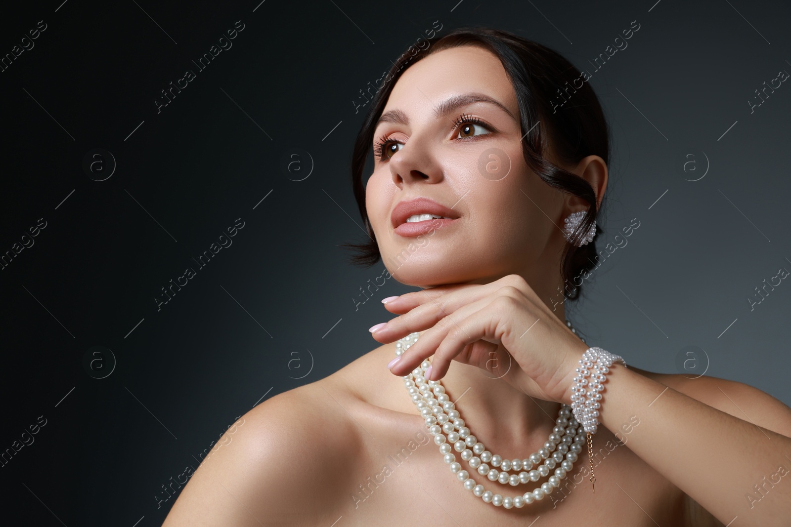 Photo of Beautiful young woman wearing elegant pearl jewelry on dark grey background