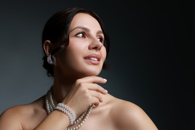 Photo of Beautiful young woman wearing elegant pearl jewelry on dark grey background. Space for text