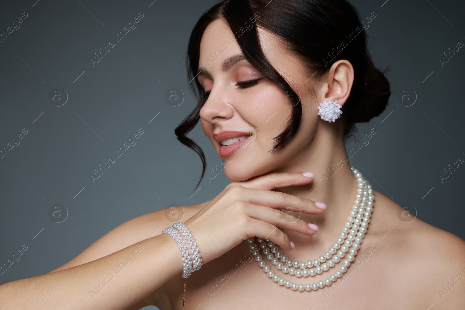 Photo of Beautiful young woman wearing elegant pearl jewelry on dark grey background