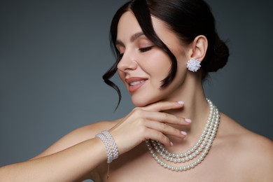 Photo of Beautiful young woman wearing elegant pearl jewelry on dark grey background