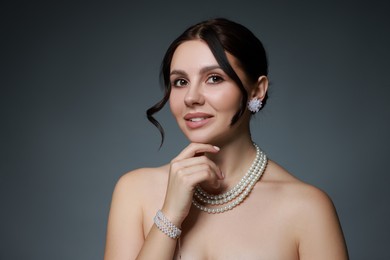 Photo of Beautiful young woman wearing elegant pearl jewelry on dark grey background