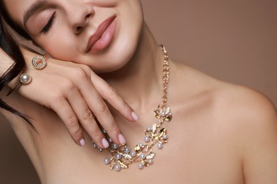 Photo of Young woman wearing elegant jewelry on brown background, closeup