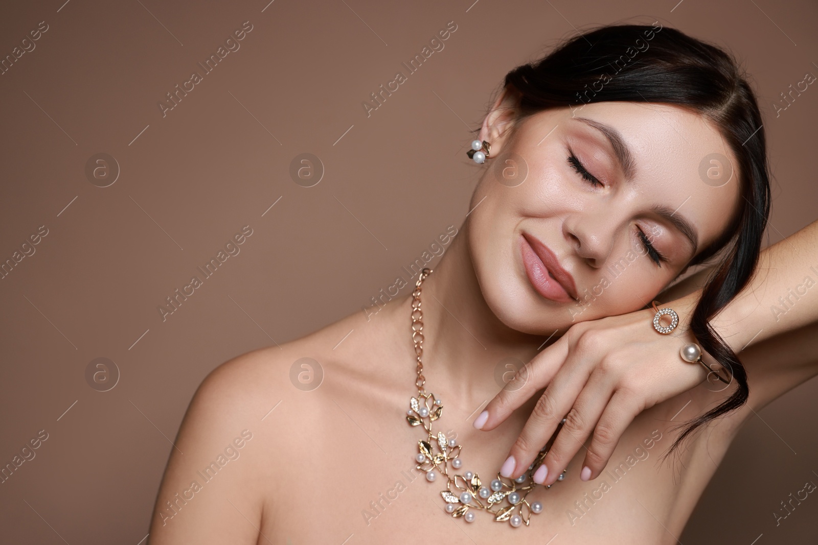 Photo of Beautiful young woman wearing elegant jewelry on brown background. Space for text