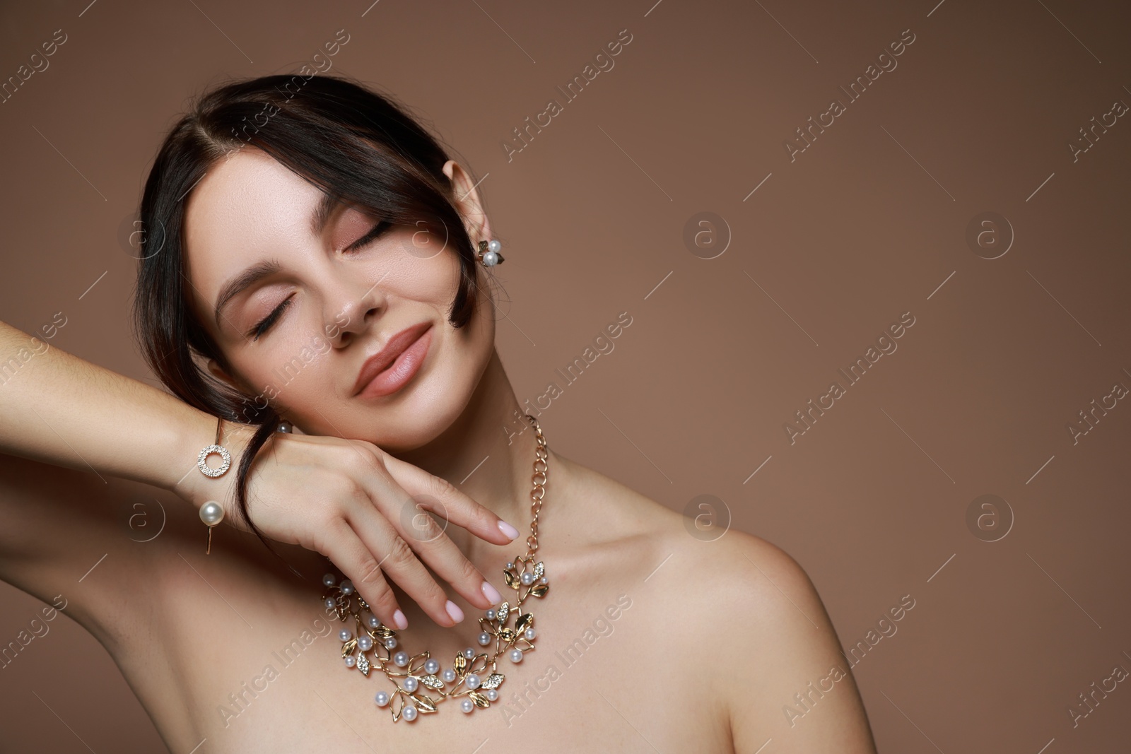 Photo of Beautiful young woman wearing elegant jewelry on brown background. Space for text