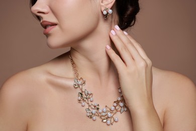 Photo of Young woman wearing elegant earrings and necklace on brown background, closeup