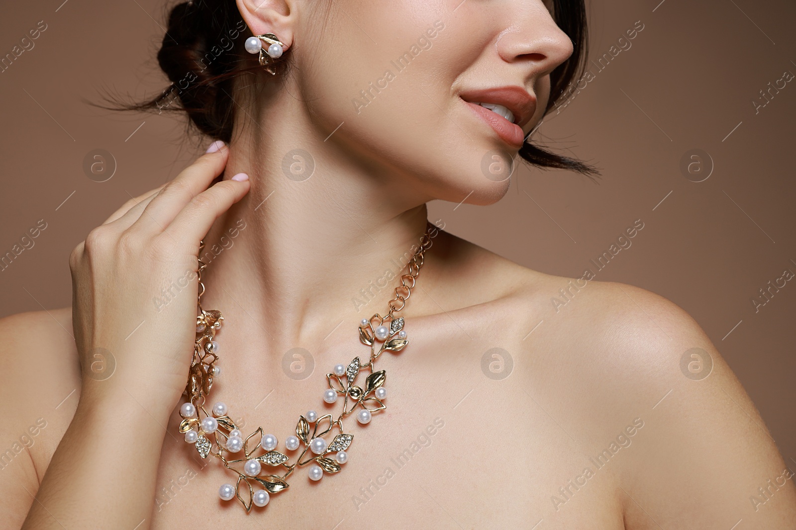 Photo of Young woman wearing elegant earrings and necklace on brown background, closeup