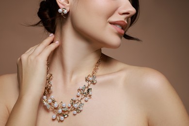 Photo of Young woman wearing elegant earrings and necklace on brown background, closeup