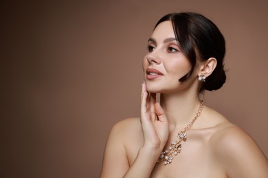 Beautiful young woman wearing elegant jewelry on brown background. Space for text