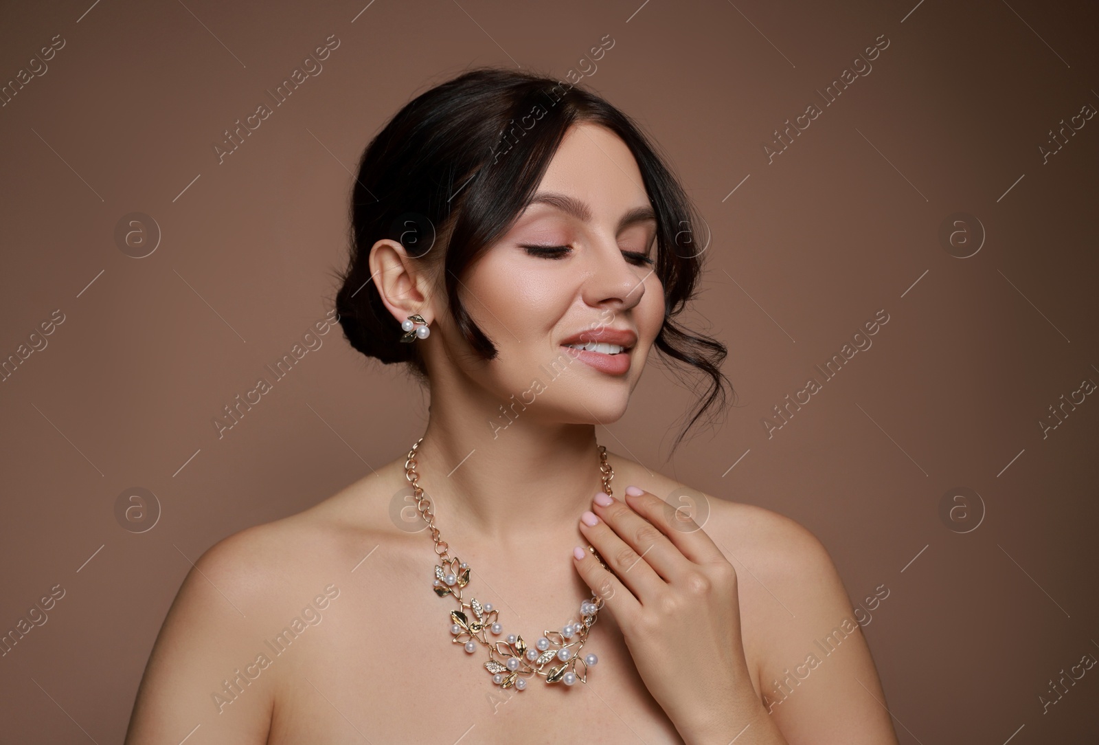 Photo of Beautiful young woman wearing elegant jewelry on brown background