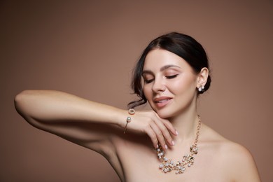 Beautiful young woman wearing elegant jewelry on brown background