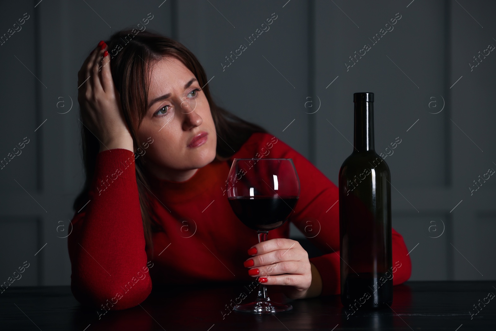 Photo of Alcohol addiction. Woman with glass of red wine and bottle at wooden table indoors