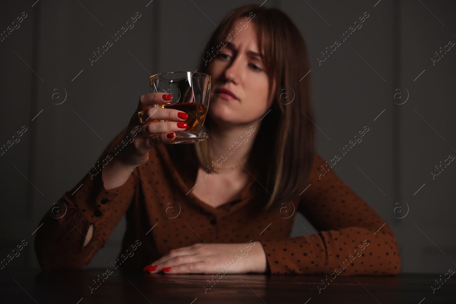 Photo of Alcohol addiction. Woman with glass of whiskey at wooden table indoors