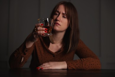 Photo of Alcohol addiction. Woman with glass of whiskey at wooden table indoors