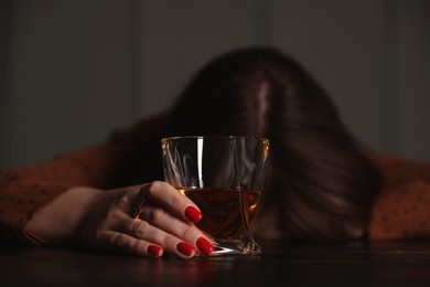 Photo of Alcohol addiction. Woman with glass of whiskey at wooden table indoors, selective focus