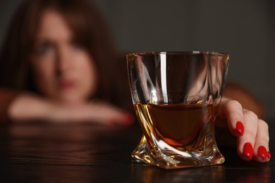 Photo of Alcohol addiction. Woman with glass of whiskey at wooden table indoors, selective focus