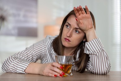 Photo of Alcohol addiction. Woman with glass of whiskey at wooden table indoors