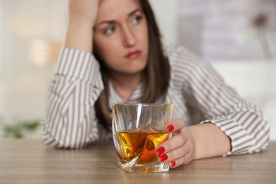 Photo of Alcohol addiction. Woman with glass of whiskey at wooden table indoors, selective focus