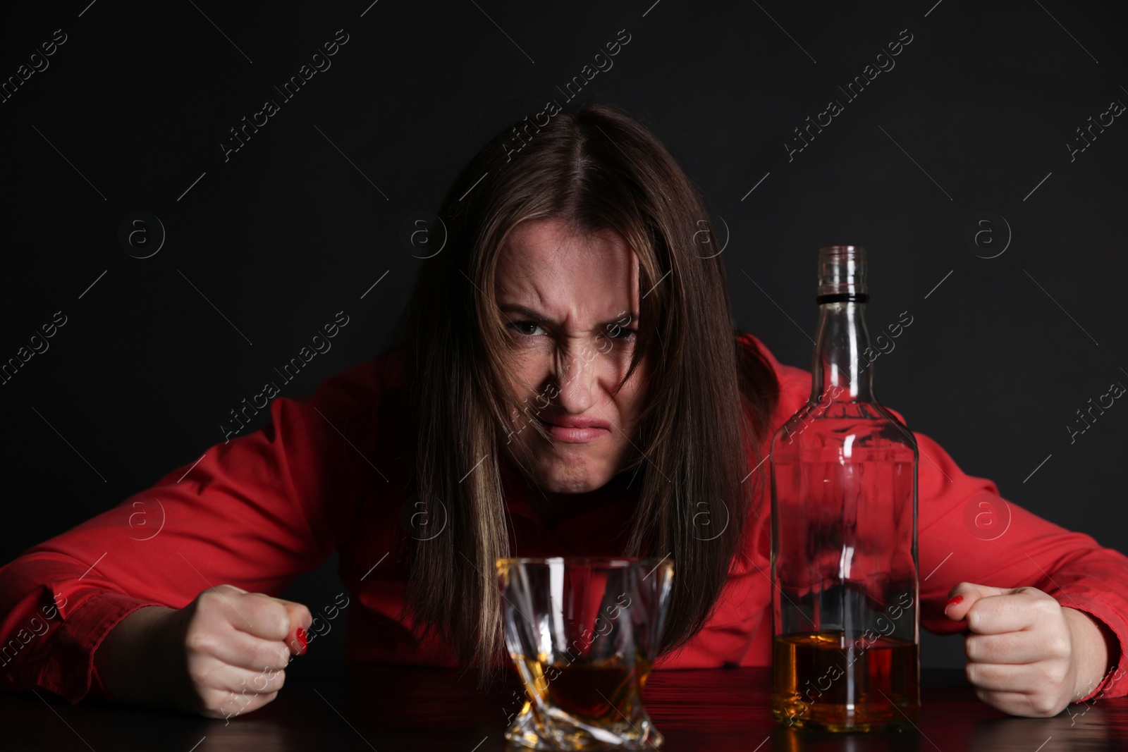 Photo of Alcohol addiction. Angry woman with whiskey at table in dark