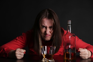 Photo of Alcohol addiction. Angry woman with whiskey at table in dark