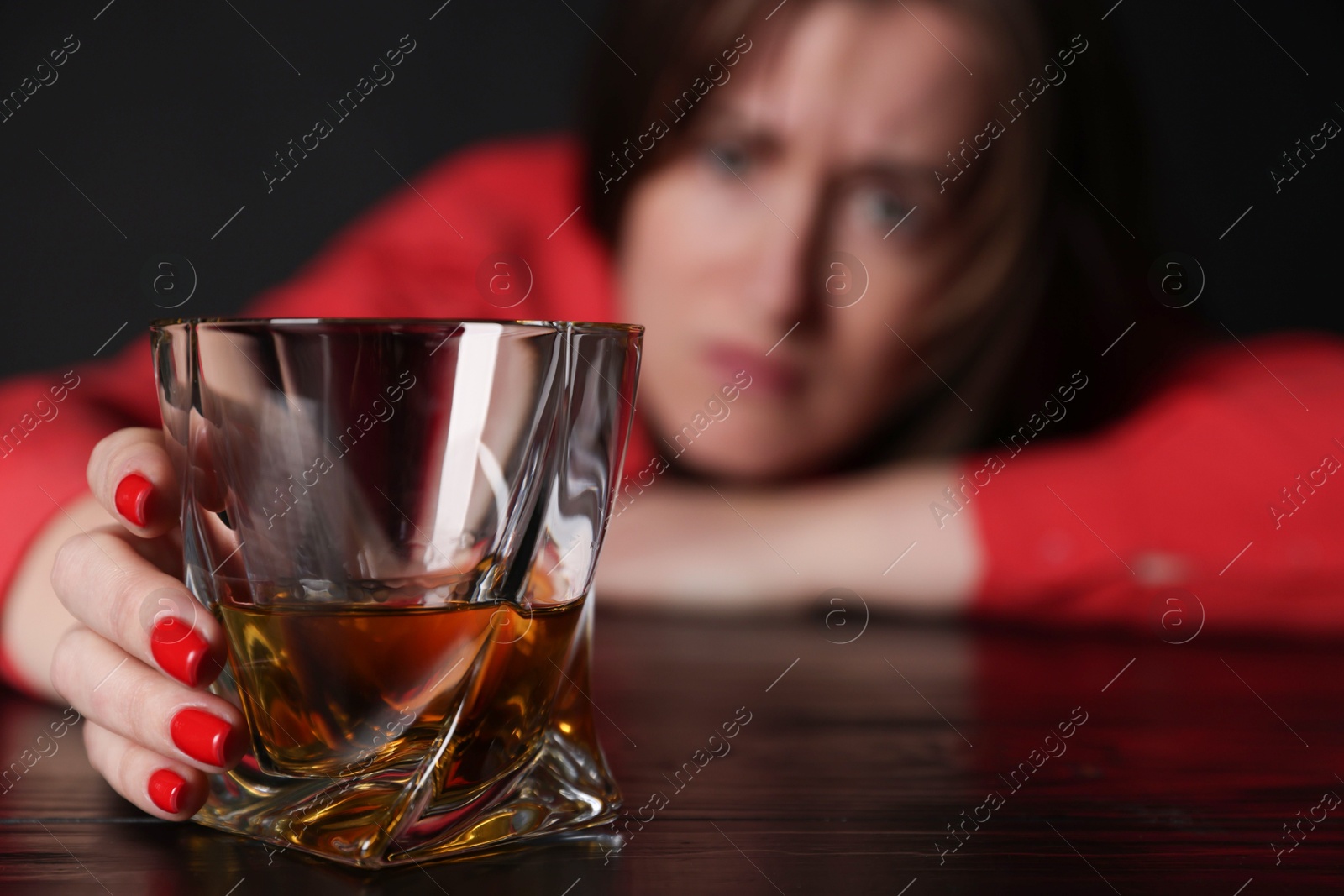 Photo of Alcohol addiction. Miserable woman with whiskey at table in dark, selective focus