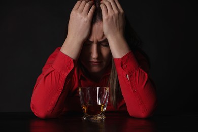 Photo of Alcohol addiction. Miserable woman with whiskey at table in dark